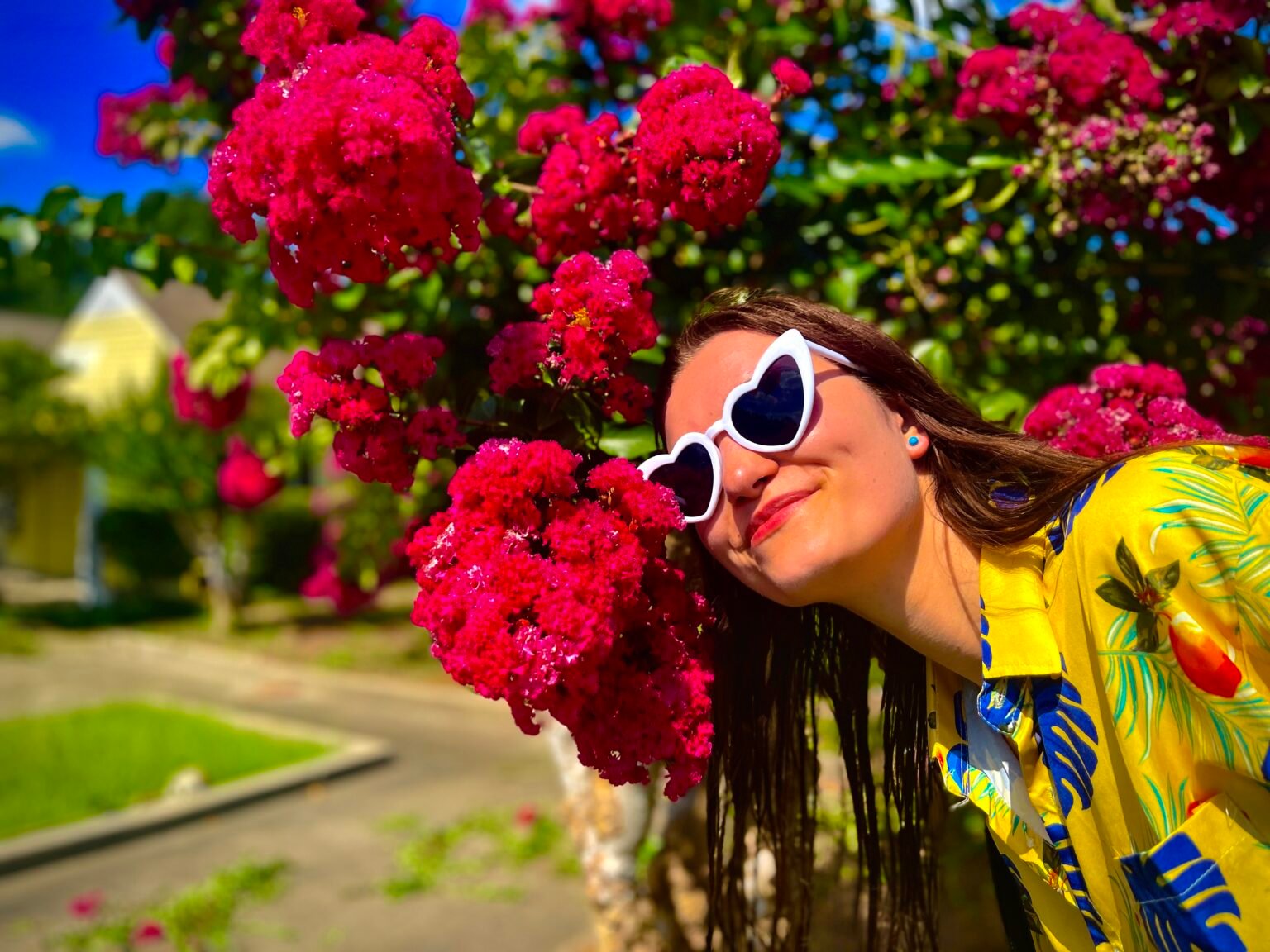 girl wearing colorful clothes, yellow shirt and white sunglasses, smiling and surrounded by vibrant pink flowers