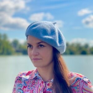 bright blue beret front view on a model, a river and clouds in the background