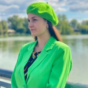 bright green beret front view on a model with brown hair, she is wearing vibrant green blazer, river and green trees in the background