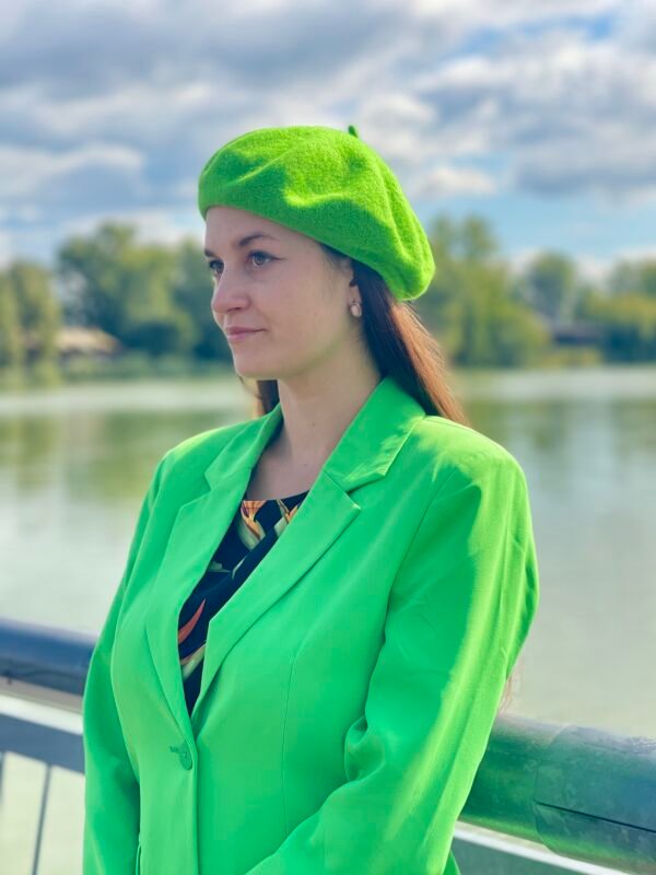 bright green beret front view on a model with brown hair, she is wearing vibrant green blazer, river and green trees in the background