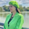 bright green beret front view on a model with brown hair, she is wearing vibrant green blazer, river and green trees in the background