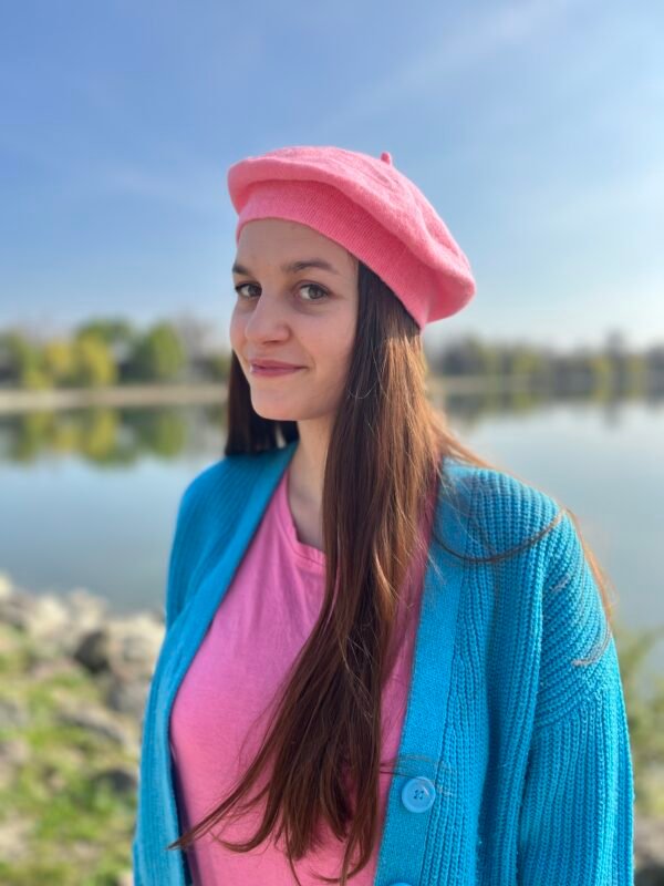 woman wearing candy pink beret and a blue cardigan, a lake in the background