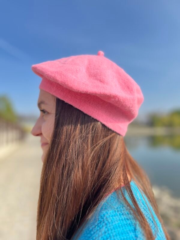 woman turned to her side wearing candy pink beret, the blue sky in the background