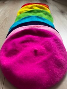 colorful berets displayed on the wooden floor - fuchsia beret, candy pink beret, purple beret, blue beret, green beret and yellow beret.