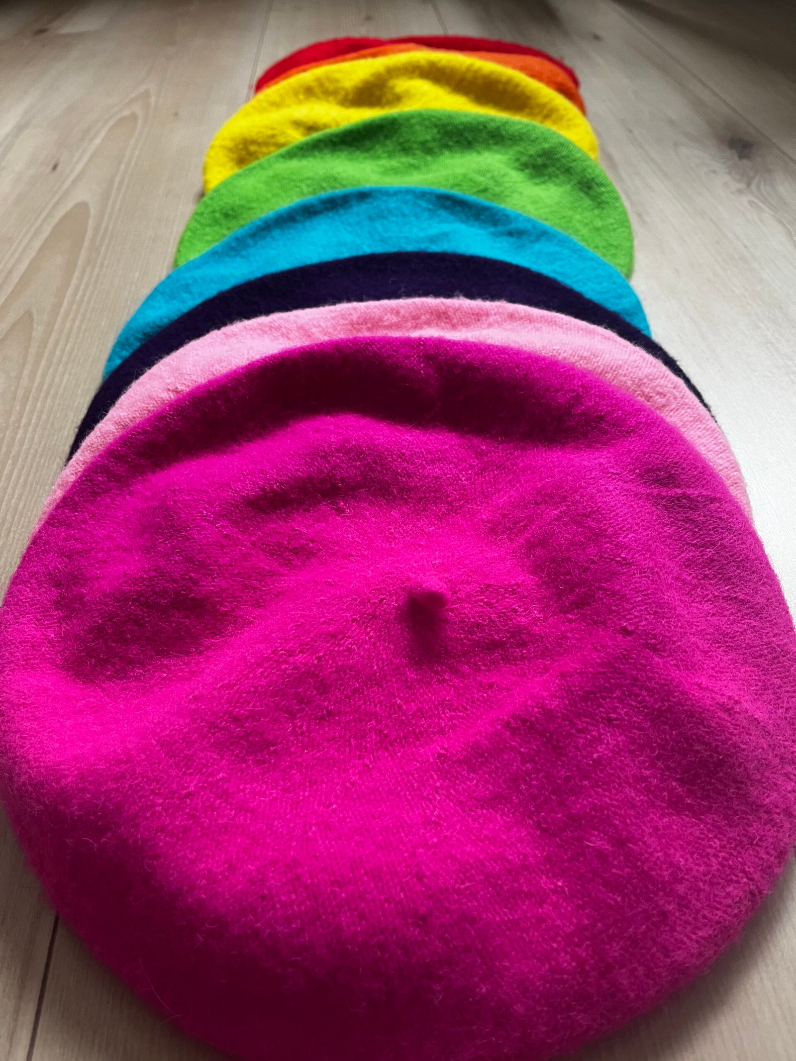 colorful berets displayed on the wooden floor - fuchsia beret, candy pink beret, purple beret, blue beret, green beret and yellow beret.