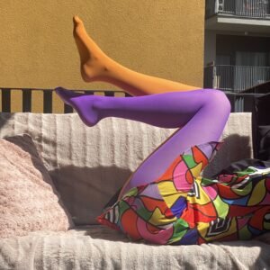 colorful tights purple and orange side view on a model's legs, she is sitting on a pale pink sofa, only her legs ae visible