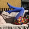 dark blue tights side view on the legs of a model, she is sitting on a pale pink sofa, only her legs are visible