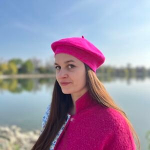 woman wearing fuchsia beret, a lake and blue sky behind her