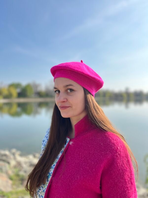 woman wearing fuchsia beret, a lake and blue sky behind her