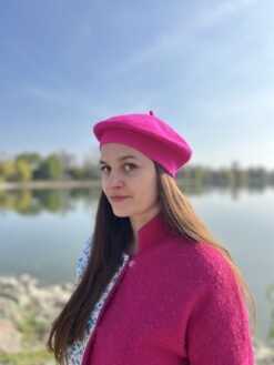woman wearing fuchsia beret, a lake and blue sky behind her