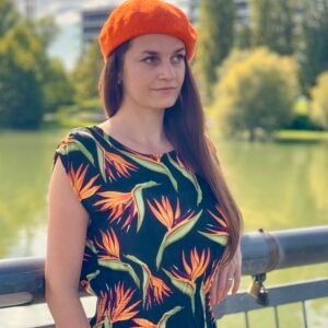 a girl with brown hear wearing orange beret, front and side view, a river and green trees in the background