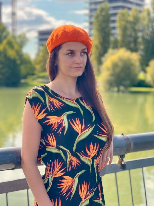 a girl with brown hear wearing orange beret, front and side view, a river and green trees in the background