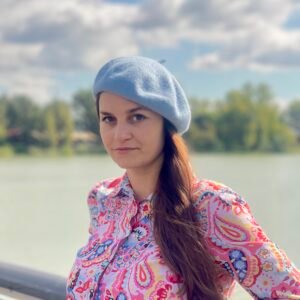 woman wearing pale blue beret and a colorful button skirt and turning to her side