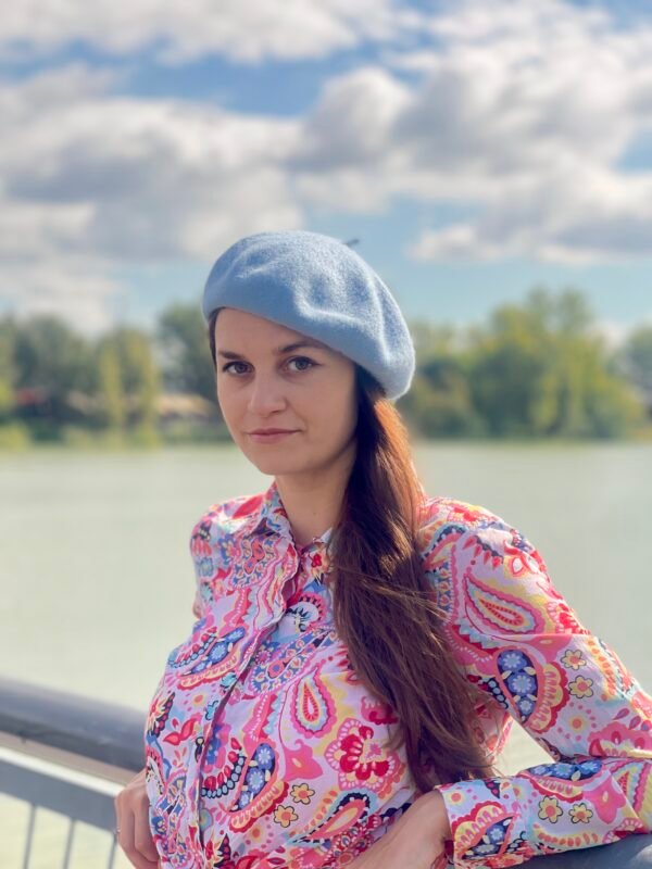 woman wearing pale blue beret and a colorful button skirt and turning to her side