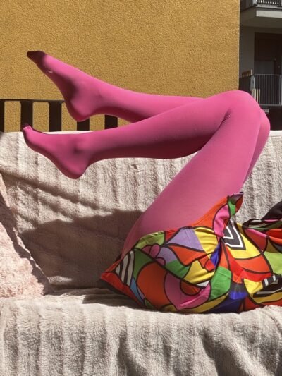pink tights side view on model's legs, she is sitting on a pale pink sofa, only her legs are visible