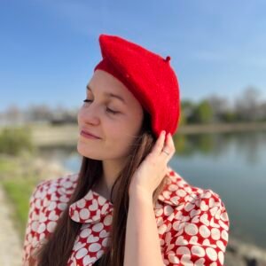 girl wearing a red beret and touching it with care, a lake in the background