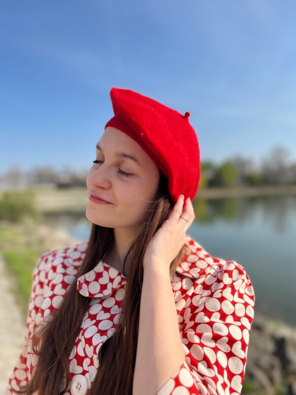 girl wearing a red beret and touching it with care, a lake in the background