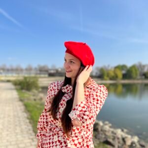 a woman wearing a red beret, red and white coat, she is smiling, an alley and a lake in the background