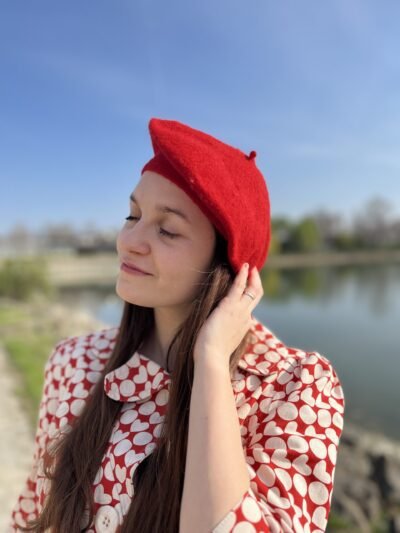 girl wearing a red beret and touching it with care, a lake in the background