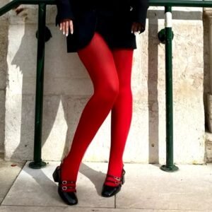 woman wearing red tights and a black coat, beige wall behind her