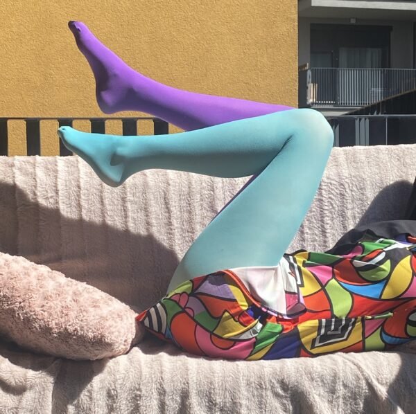 woman lying on a pink sofa and wearing two color colorful tights, they are blue and purple