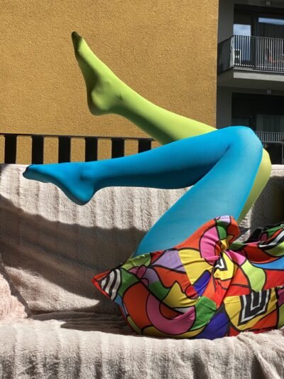 woman lying on a pink sofa wearing two colors colorful tights, blue and green variation