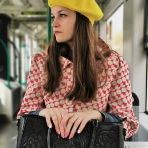 yellow beret side view on a model, she is wearing red and white coat and holding a black purse