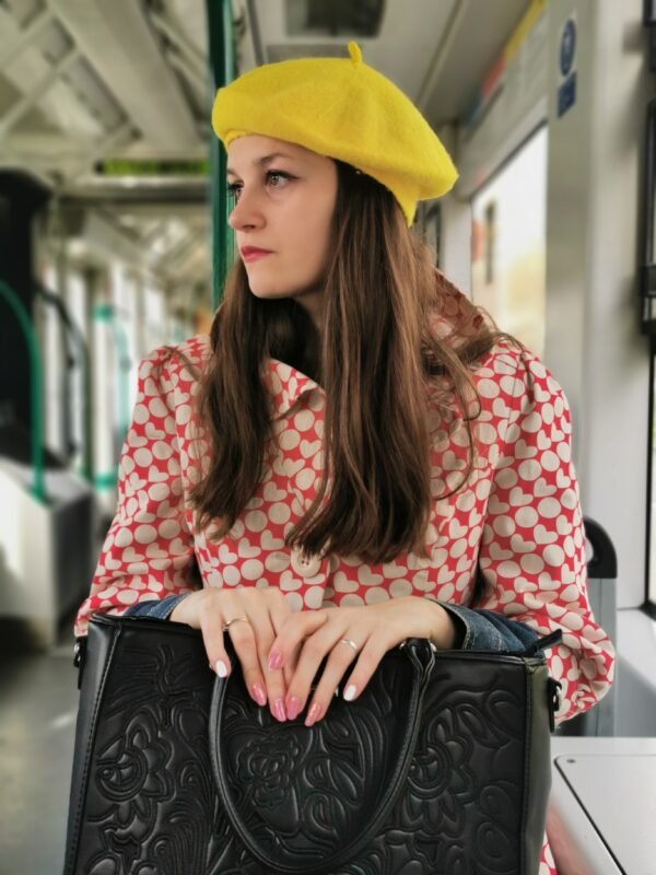 yellow beret side view on a model, she is wearing red and white coat and holding a black purse