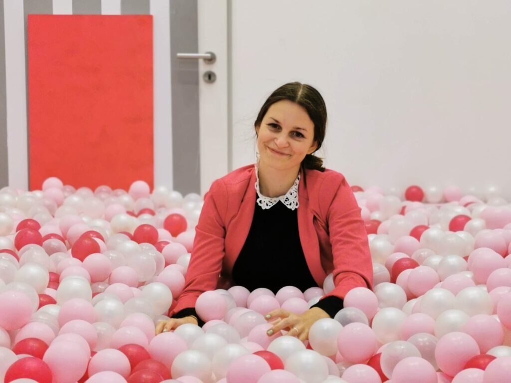 woman wearing colorful clothes and siting on a pool full of pink plastic balls