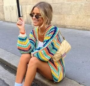 woman wearing long sleeve colorful cardigan and holding a beige bag