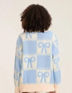 woman with curly brown hair turned to her back wearing blue colorful sweater with ribbons