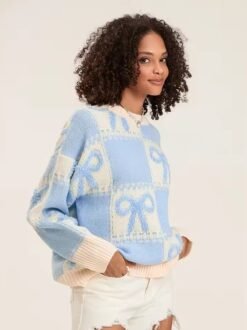 woman with curly brown hair turned to her side wearing blue colorful sweater with ribbons and white shorts