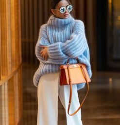 woman wearing blue colorful turtleneck sweater, white pants and holding an orange pants