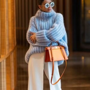 woman wearing blue colorful turtleneck sweater, white pants and holding an orange pants