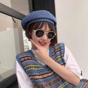 woman wearing blue plaid colorful beret and a crochet sweater and sunglasses, a window behind her