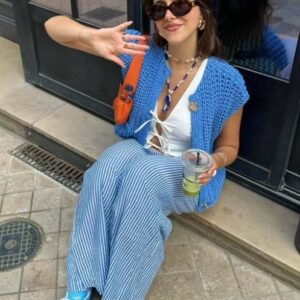 woman wearing blue sleeveless cardigan, white top and jeans, grey concrete under her