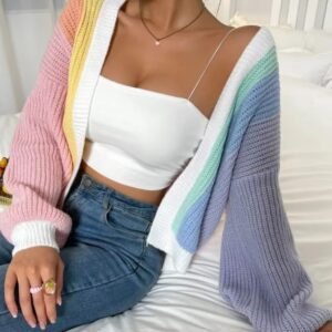 woman wearing casual colorful cardigan, white top and dark jeans, she is sitting on the white bed