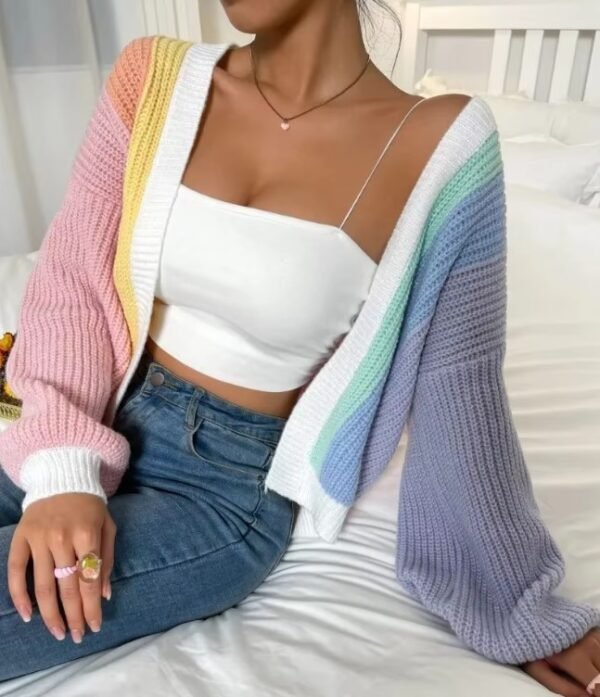 woman wearing casual colorful cardigan, white top and dark jeans, she is sitting on the white bed