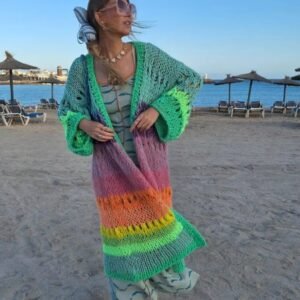 woman wearing colorful Bohemian cardigan and a green dress, she has a blue ribbon in her hair, beach in the background