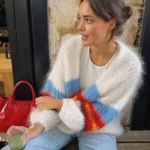 woman wearing colorful fuzzy cardigan, jeans and holding a red bag, she is drinking matcha