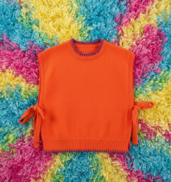 orange sleeveless sweater placed on a vibrant colorful carpet