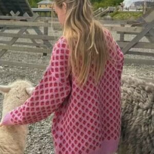 blonde woman turned to her back wearing colorful strawberry sweater and tending to sheep