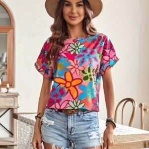 woman with brown hair wearing colorful summer blouse, jeans shorts and a summer hat, bright room behind her