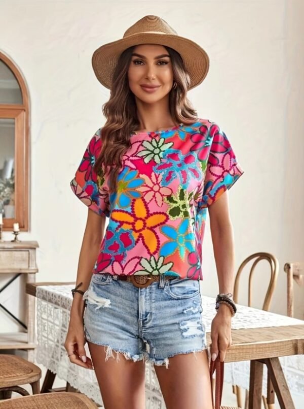 woman with brown hair wearing colorful summer blouse, jeans shorts and a summer hat, bright room behind her