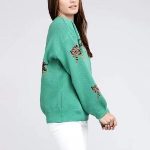 woman turned to her side wearing green colorful tiger print sweater and white pants