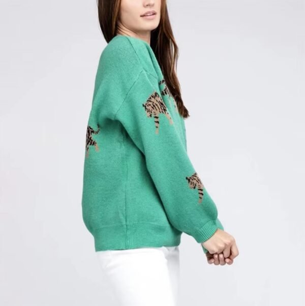 woman turned to her side wearing green colorful tiger print sweater and white pants