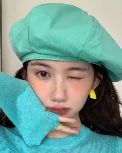 woman with black hair wearing colorful womens beret and winking