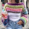 woman wearing cropped colorful sweater and a white shirt, she is holding a pink drink