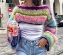 woman wearing cropped colorful sweater and a white shirt, she is holding a pink drink
