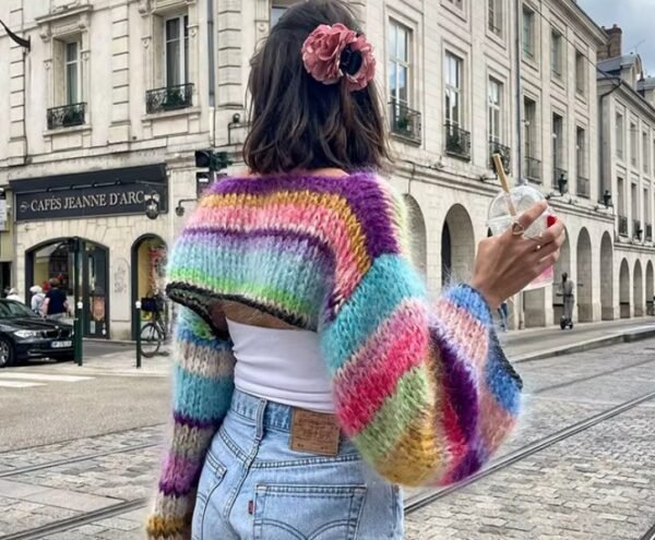 woman turned to her back wearing cropped colorful sweater and having a pink scrunchie in her hair, the street in the background